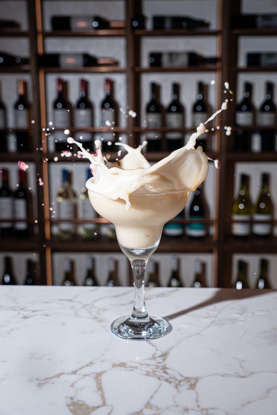 Cream cocktail splashing with rose petals against a wine wall
