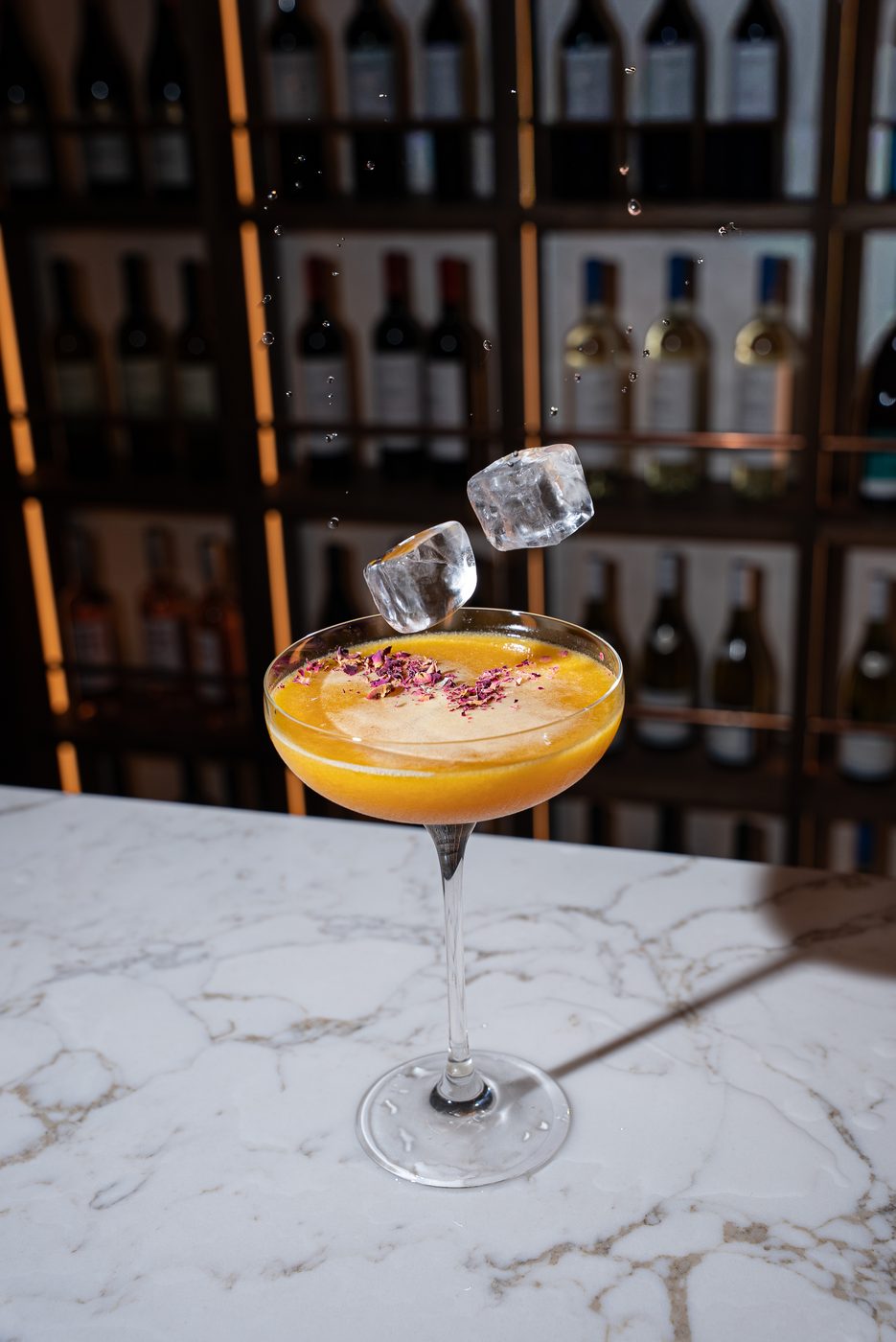 Golden cocktail with rose petals and falling ice cubes