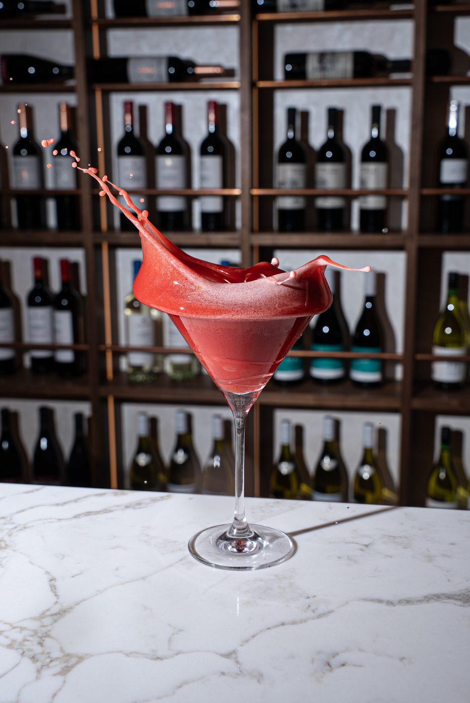 Red cocktail splashing in a martini glass on a marble bar
