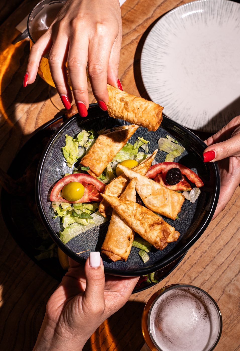 Hands sharing crispy spring rolls and mezze at a restaurant table